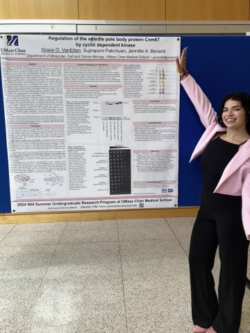 Grace Van Etten '27, in black pants, black top and pink blazer, shows off her poster at the UMass Chan Medical School Summer Undergraduate Research Program.