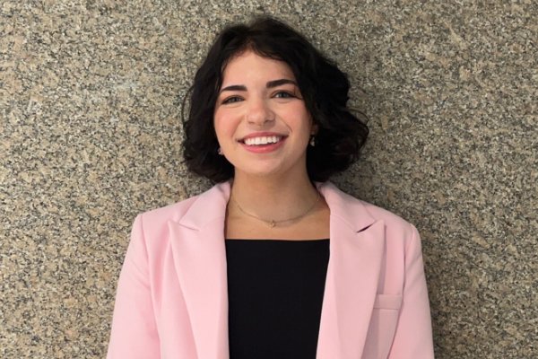 Grace VanEtten '27 in black top and pink blazer, stands against a stone wall.